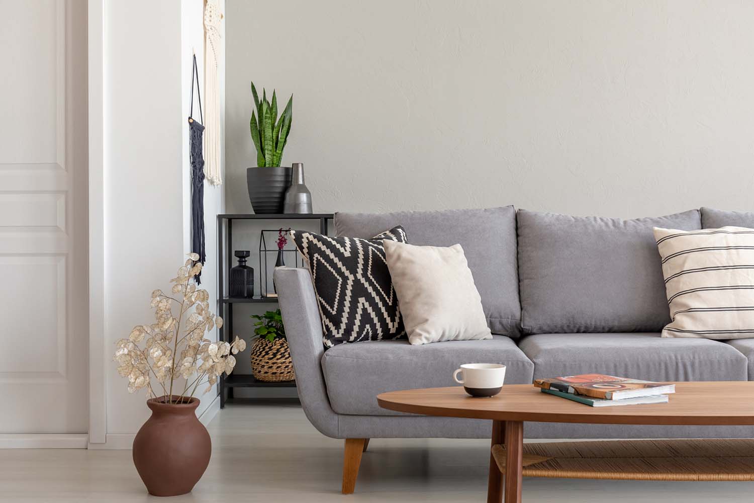 Flowers next to grey couch with pillows in minimal living room interior with wooden table.